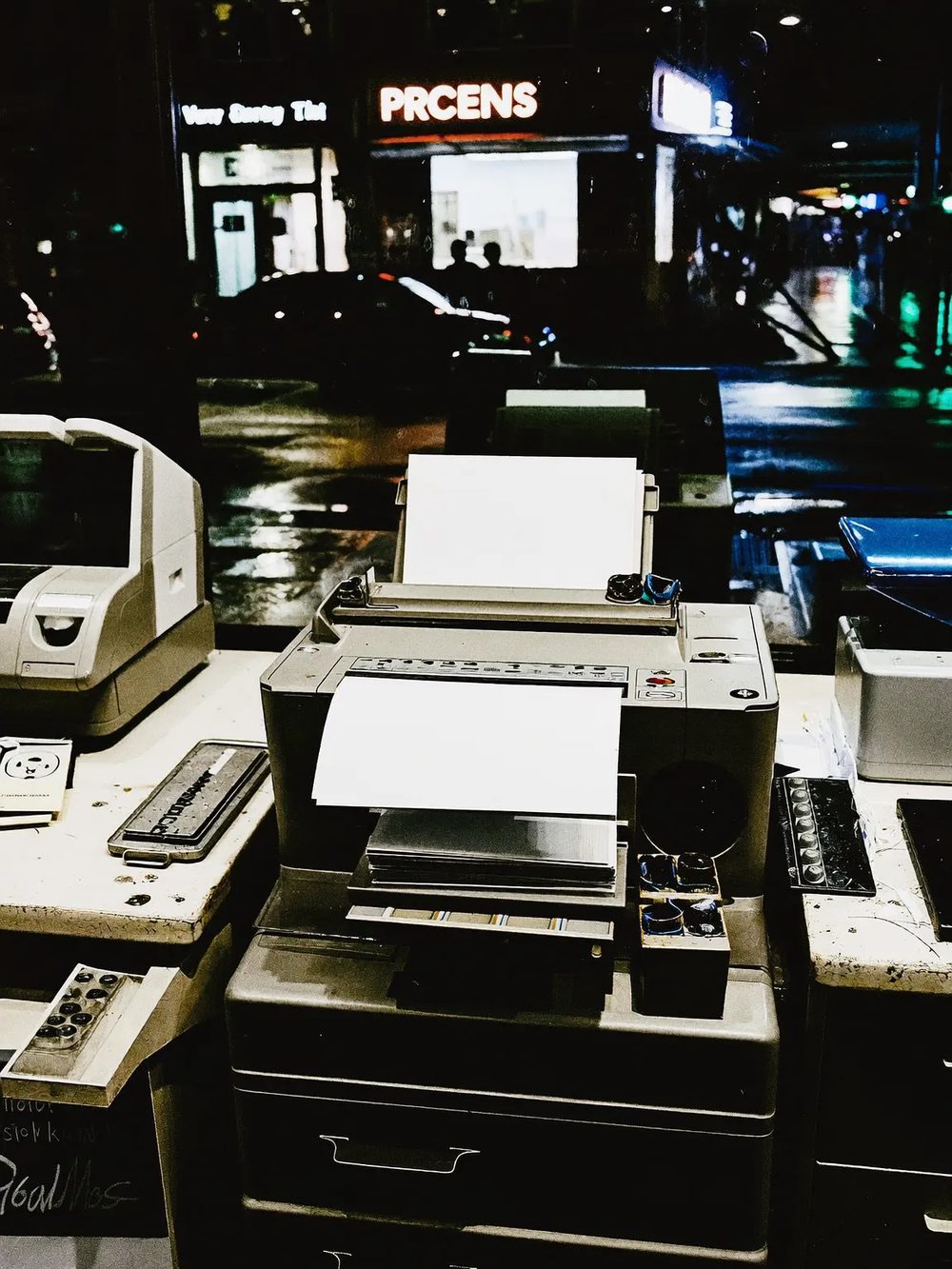 A printer running a job on the counter, trimmed sheets stacked beside it.